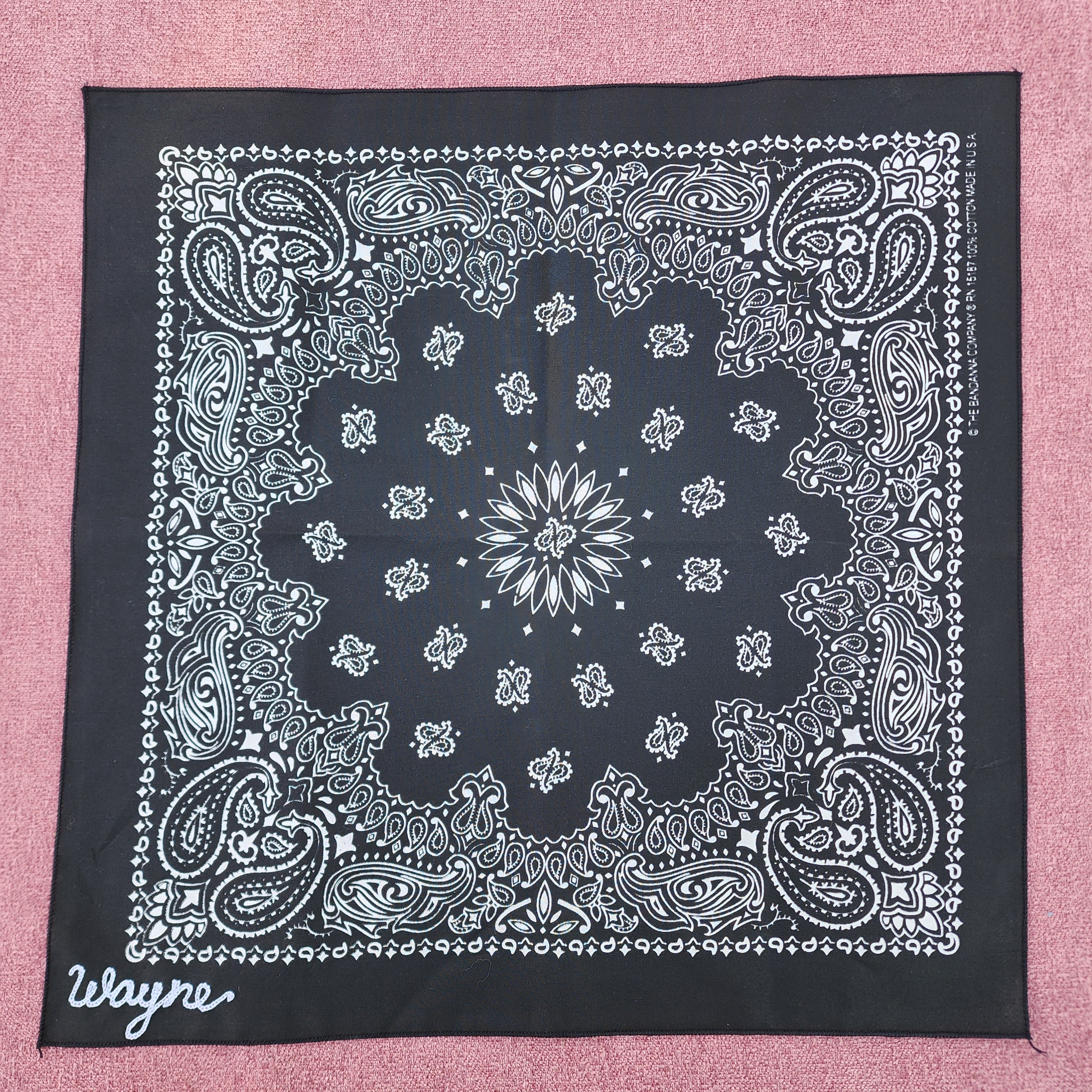 Black bandana with white paisley pattern on a pink background