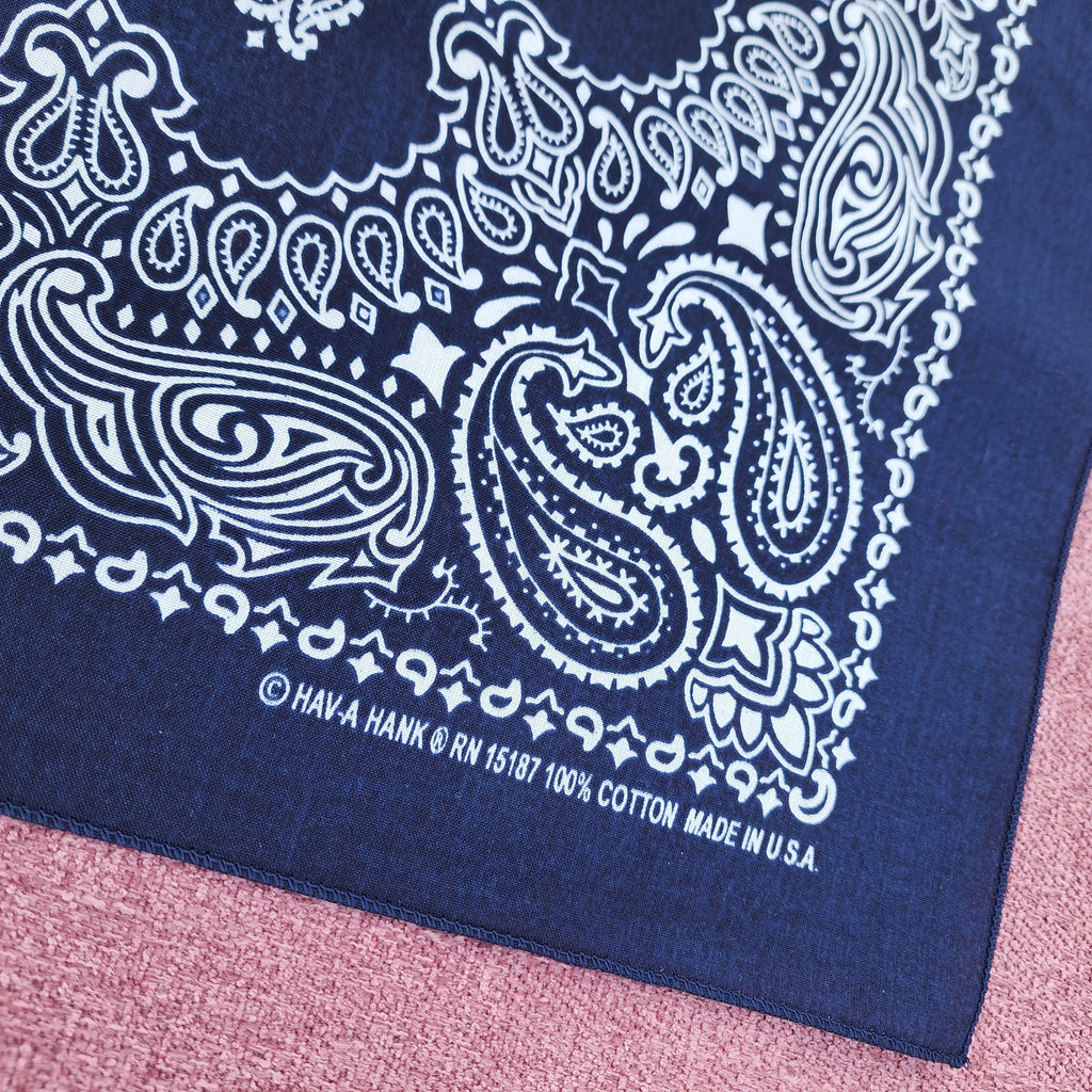 Navy blue bandana with white paisley pattern on a pink textured surface