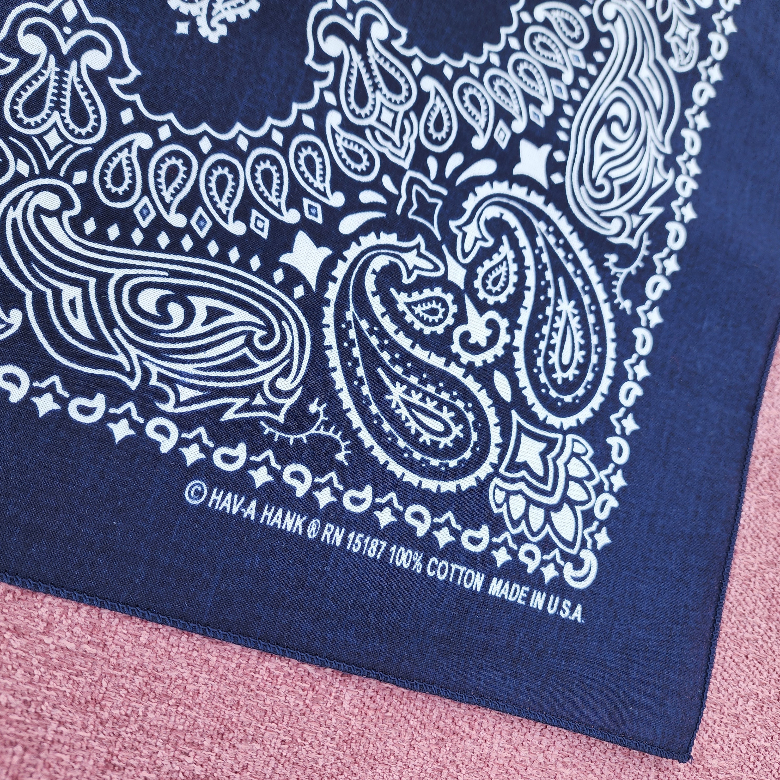 Navy blue bandana with white paisley pattern on a pink textured surface