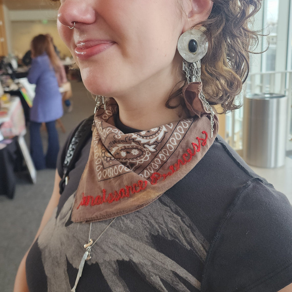 Person wearing a bandana that says Renaissance Princess with a blurred indoor background